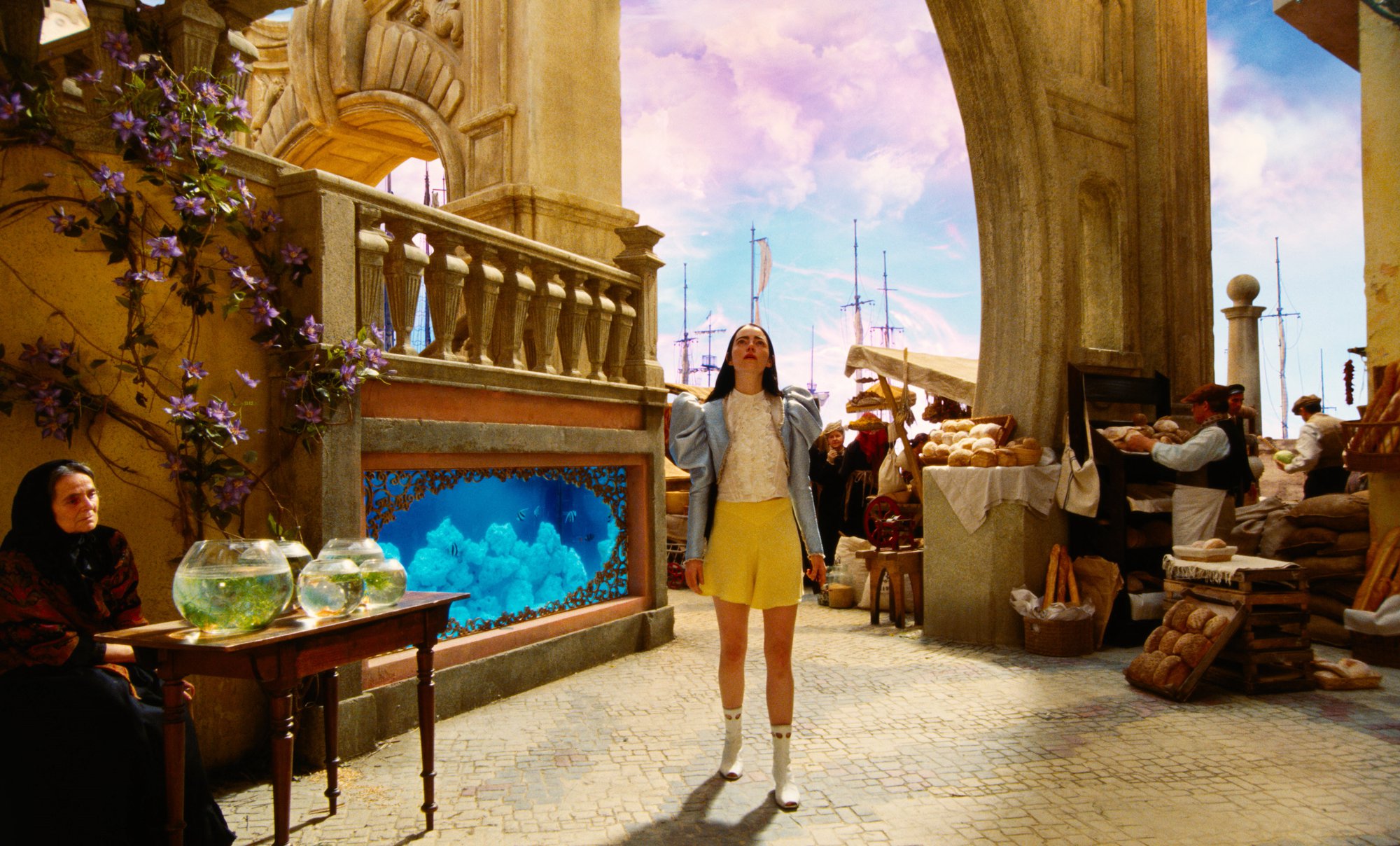 Emma Stone in 'Poor Things' standing in a market looking at the ceiling